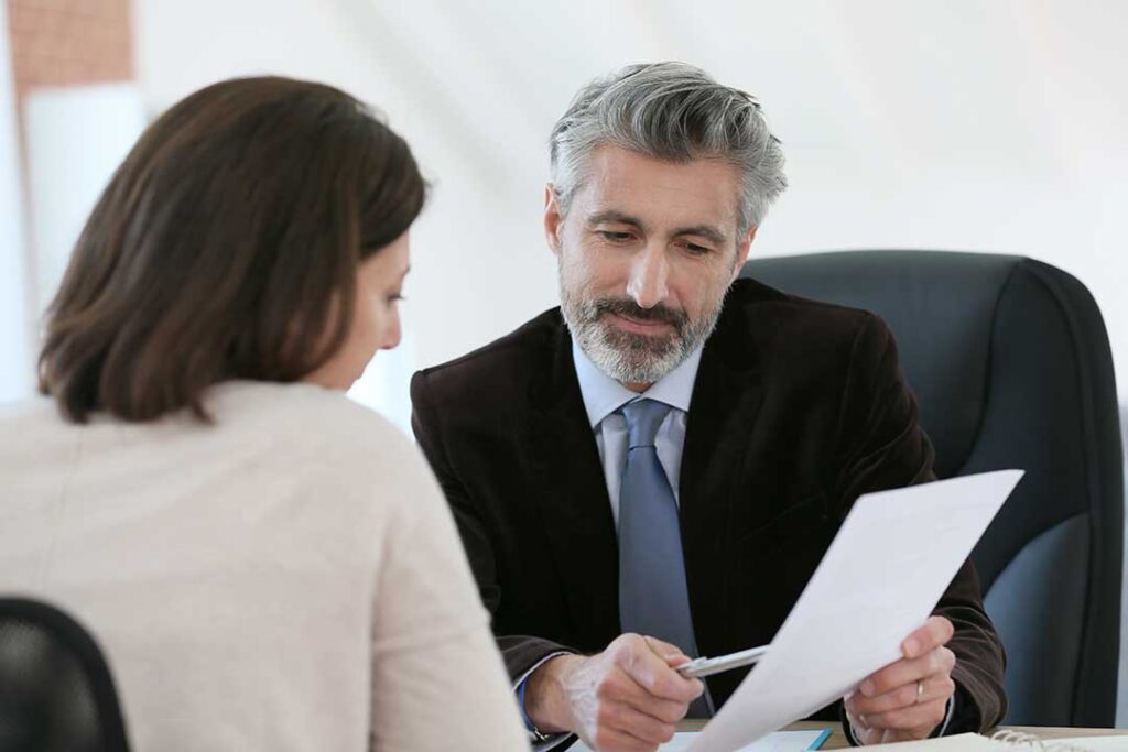 An attorney speaks privately with a person in a courthouse interview room beside arrest paperwork.