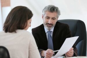 An attorney speaks privately with a person in a courthouse interview room beside arrest paperwork.